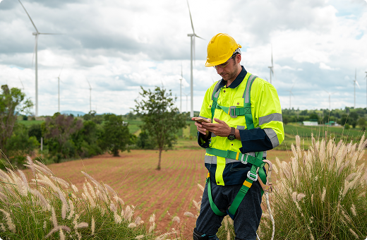 A surveyor standing in a field looking at his phone with wind turbines