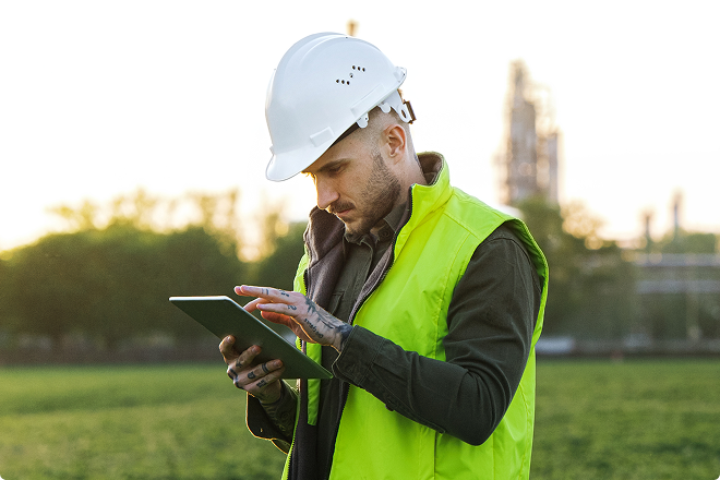 A male engineer wearing a hard hat and high-vis jacket working on a tablet